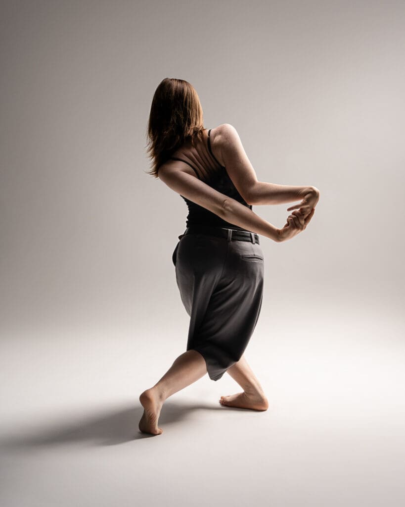 Contemporary dancer facing backwards with arms bent in odd shape.