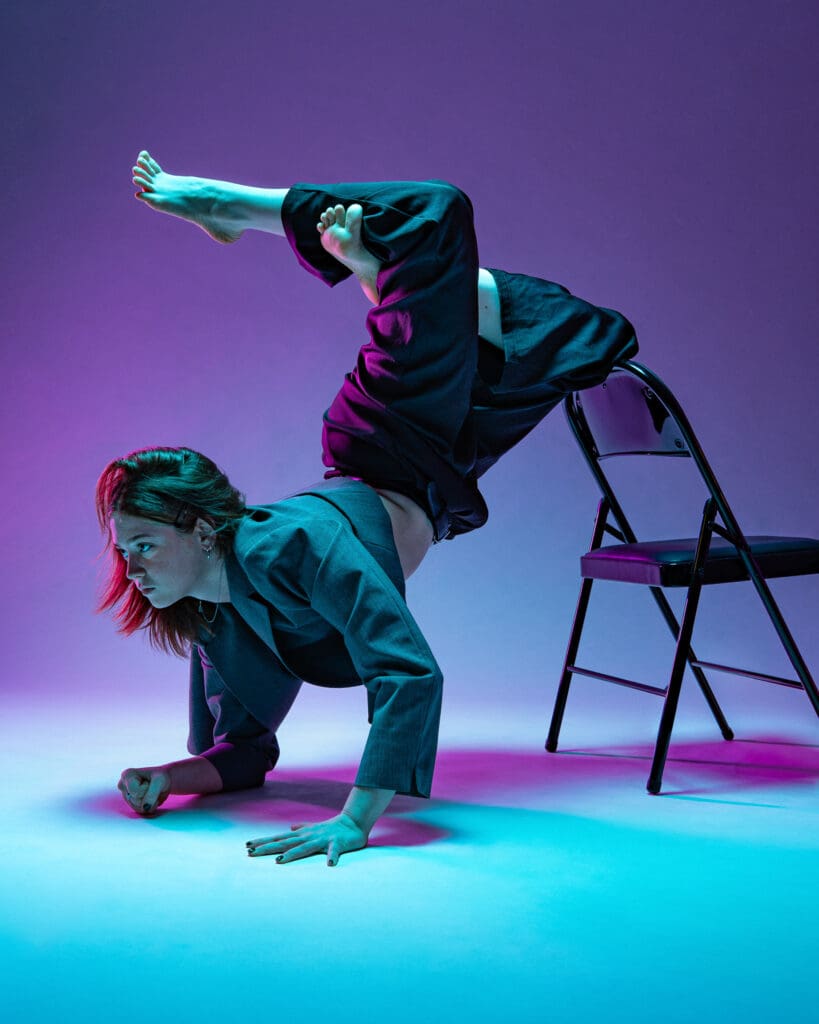 Contemporary dancer leaning forward on chair with legs propped up.