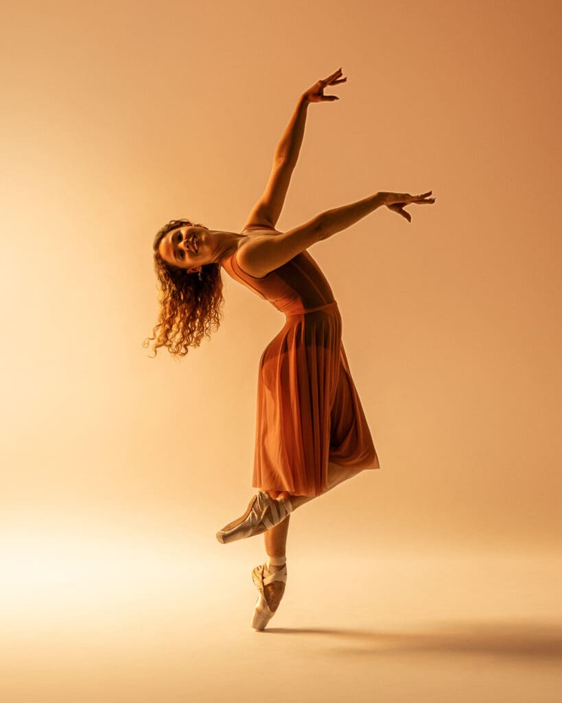 Ballet dancer on pointe shoes executes a pose on pointe with arms extended.