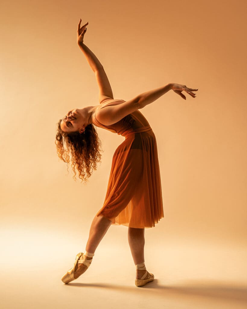 Ballet dancer with pointe shoes leans back and extends arms.