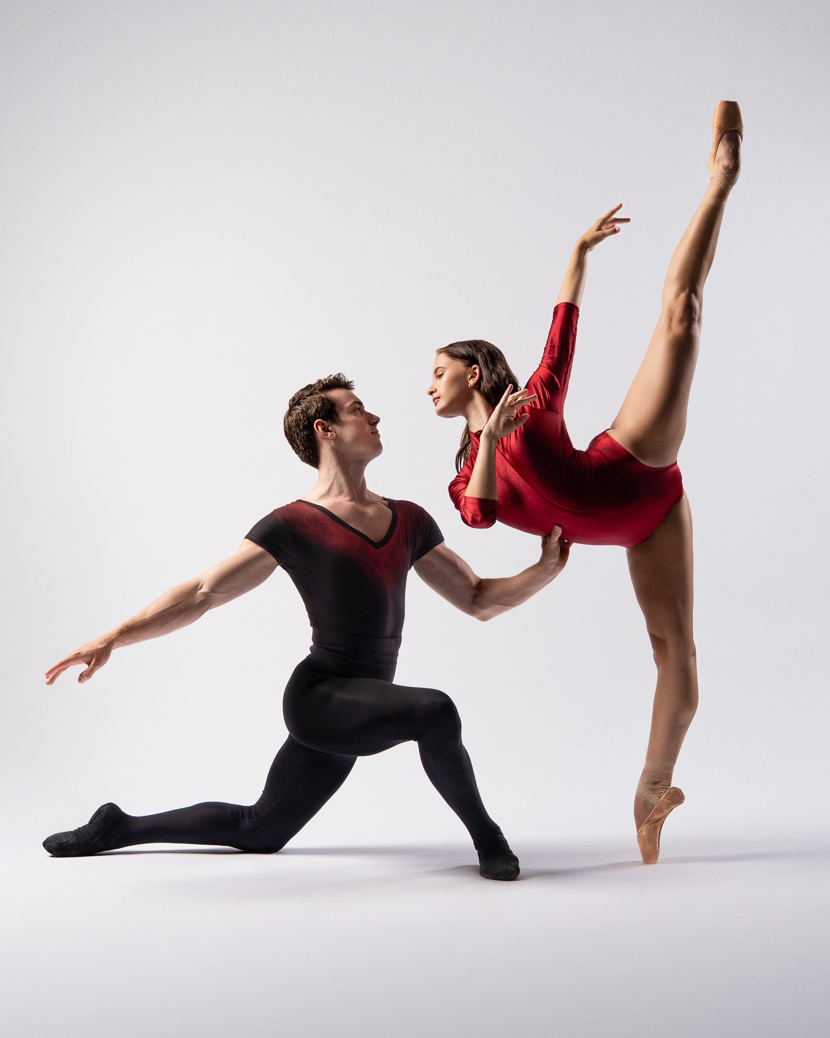 A male ballet dancer supports a female dancer in arabesque penché during a guided dance portrait session in San Antonio against a white background