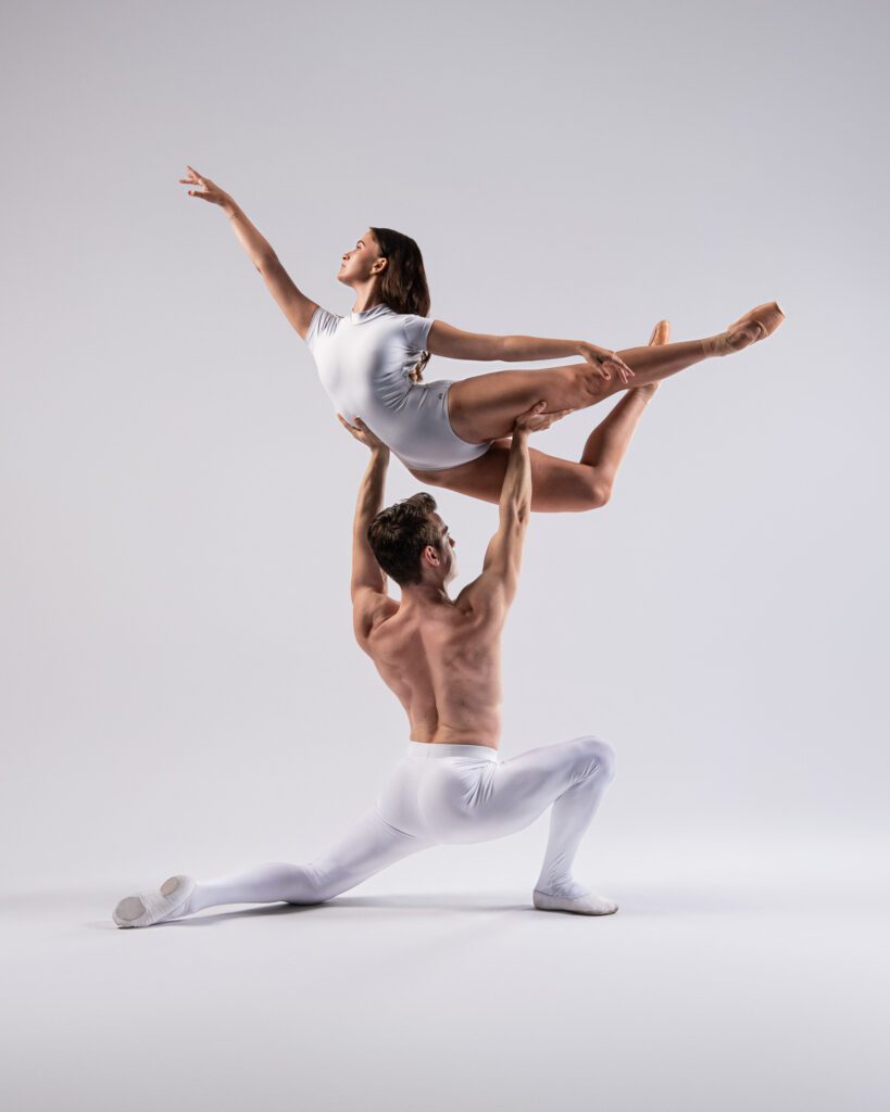 Two dancers perform an overhead lift during a dance session in San Antonio, both wearing white ballet attire against a plain background